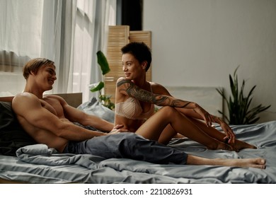 Smiling Man In Pajama Pants Looking At Seductive Girlfriend On Bed