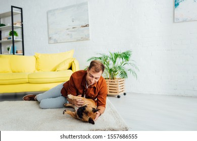 Smiling Man Playing With French Bulldog On Floor In Living Room