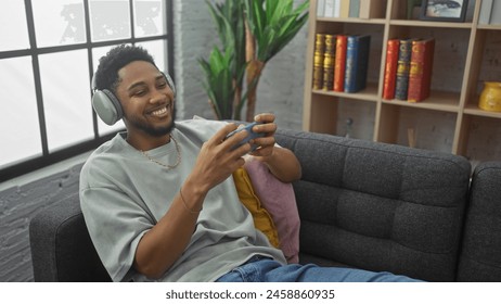 Smiling man playing mobile game on couch indoors with headphones - Powered by Shutterstock