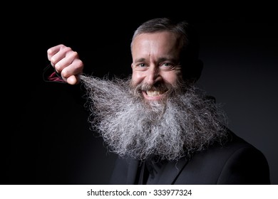 A Smiling Man Plays With His Huge Grey Beard On A Black Background