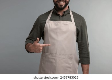 Smiling man pointing at kitchen apron on grey background, closeup. Mockup for design