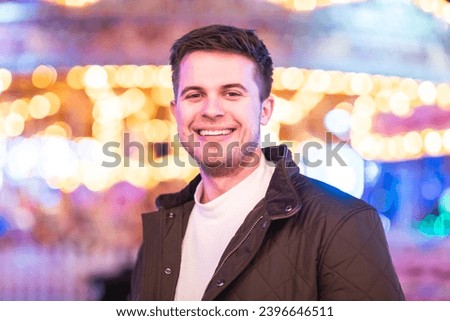 Smiling man portrait at amusement park looking at camera and smiling - young man having fun on a night out at fun fair