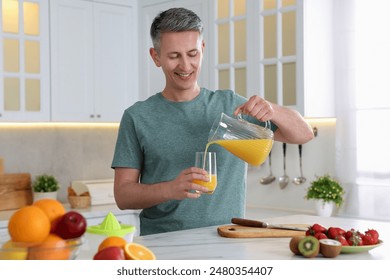 Smiling man pouring fresh orange juice into glass at white marble table in kitchen - Powered by Shutterstock