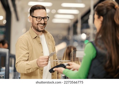 A smiling man is purchasing with credit card on pos terminal at checkout. - Shutterstock ID 2273566775