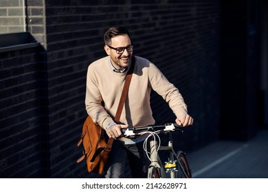 A Smiling Man Pushing A Bicycle Uphill On The City Street.