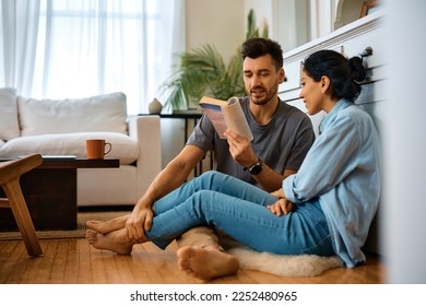 Smiling man reading book to his wife while spending time together at home.