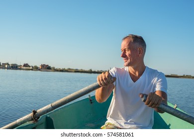 Smiling man is rowing on a small boat in a calm sea, quiet sunny morning on the coast. - Powered by Shutterstock