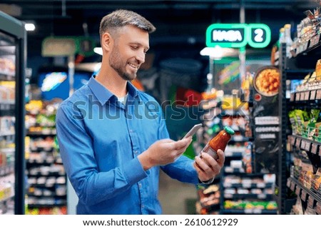 Smiling man scanning qr code on glass jar with smartphone, supermarket male customer using an online application and scanning barcode of products