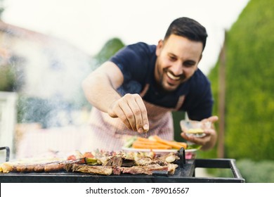 Smiling man seasoning meat on the grill