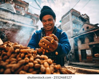 Smiling man selling peanuts outdoors, wearing a beanie and blue jacket, urban backdrop with rustic buildings. - Powered by Shutterstock