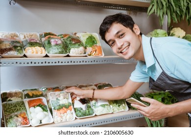 Smiling man selling vegetables holding a smartphone while checking vegetables