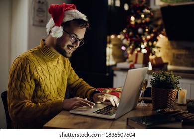 Smiling man sending e-mails on laptop on Christmas Eve at home.  - Powered by Shutterstock