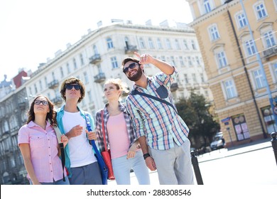 Smiling Man Showing Something To Friends On City Street