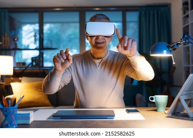 Smiling man sitting at desk and working with virtual reality, he is wearing a VR headset and interacting with virtual screens