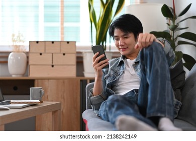 Smiling Man Sitting On Couch And Using Smart Phone, Spending Time In Social Media Internet At Home.