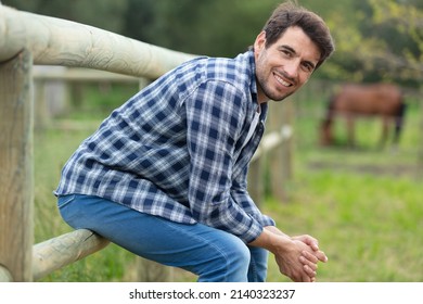 smiling man sitting on a fence in rural countryside farm