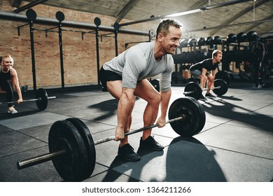 Smiling man in sportswear preparing to lift barbells during a weightlifting class in a gym