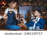 Smiling man in a suit engages with a waitress, using a card for payment, reflecting a casual yet professional dining transaction in a cafe setting.