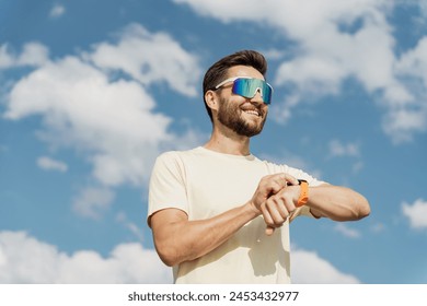 A smiling man with sunglasses looks at his watch against a bright blue sky, exuding positivity and readiness.

 - Powered by Shutterstock