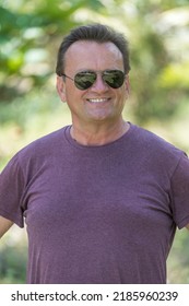 Smiling man in sunglasses outdoors portrait, close up. Middle aged man in purple shirt on nature summer background