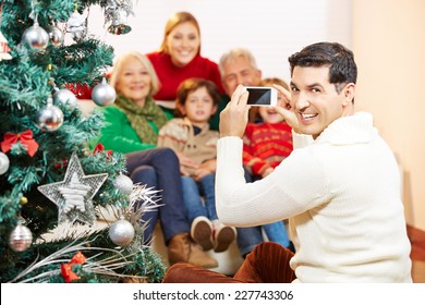 Smiling Man Taking Family Picture At Christmas With His Smartphone Camera