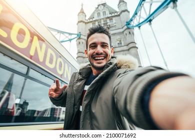 Smiling man taking selfie portrait during travel in London, England - Young tourist male taking memory pic with iconic england landmark - Happy people wandering around Europe concept - Shutterstock ID 2100071692