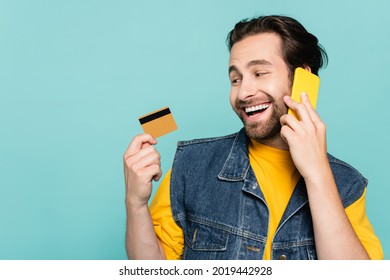 Smiling Man Talking On Mobile Phone And Looking At Credit Card Isolated On Blue