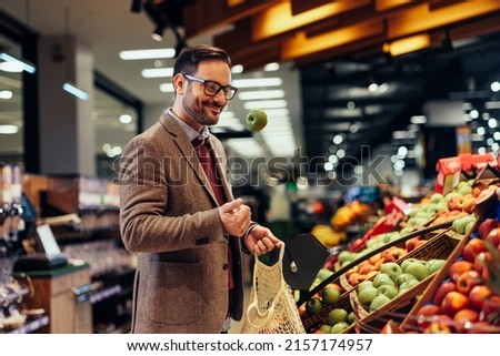 Smiling man throws in the air while standing by groceries (fruit and vegetables) department in the supermarket