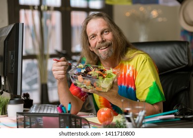 Smiling Man In Tie Dye Shirt Eating Healthy Food At His Desk