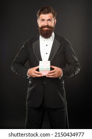 Smiling Man In Tuxedo Bow Tie Formalwear On Black Background With Gift Box. Boxing Day