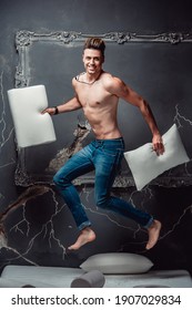 Smiling man with two white pillows in hands jumping on a mattress on a gray background. Concept of comfortable sleep. orthopedic mattress and pillow