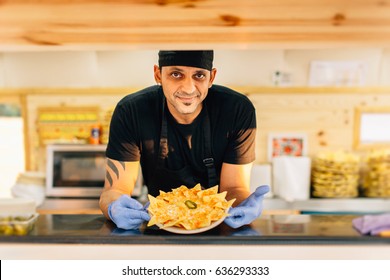 Smiling man in uniform smiling at camera and showing order standing in food truck. - Powered by Shutterstock