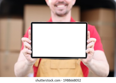 Smiling Man In Uniform Holds Tablet With White Screen In Background Of Cardboard Boxes