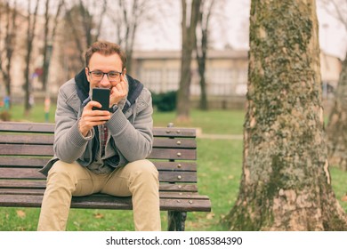 Smiling man using cellphone while sitting on the bench.