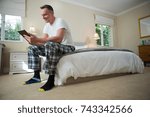 Smiling man using digital tablet on bed in bedroom at home
