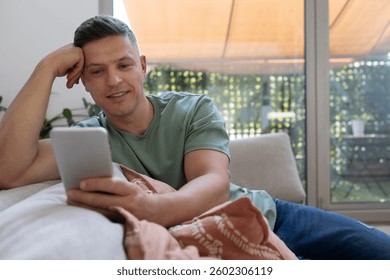 Smiling man using digital tablet while relaxing on comfortable sofa at home
