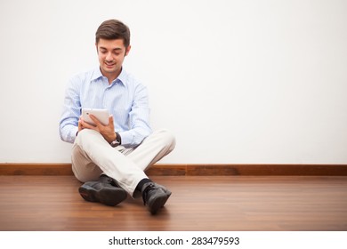 Smiling man using a digital tablet while sitting on the floor of his apartment