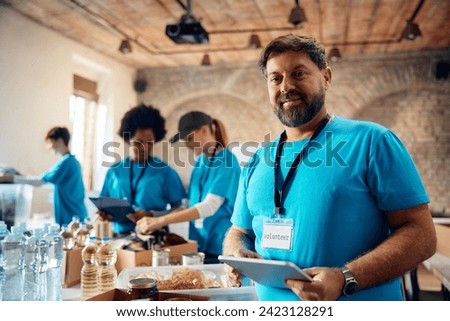 Smiling man using digital tablet while volunteering at community center and looking at camera.