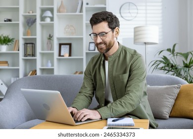 Smiling man using laptop while working from home in a modern, cozy living room with a stylish interior. - Powered by Shutterstock