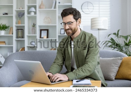 Smiling man using laptop while working from home in a modern, cozy living room with a stylish interior.