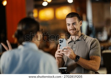 Smiling man using smartphone to capture a moment with a woman in a restaurant or coffee shop. Enjoying date