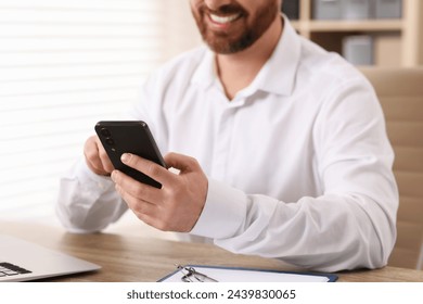 Smiling man using smartphone at table in office, closeup