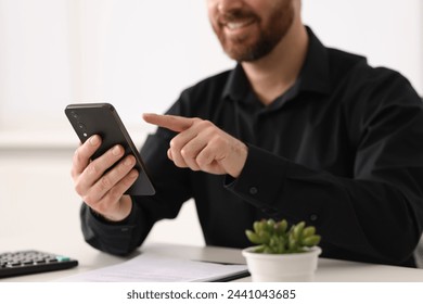 Smiling man using smartphone at table in office, closeup