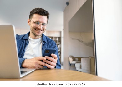 Smiling man using smartphone while sitting at a table in a modern workspace during daylight