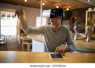 Smiling man using virtual reality headset and digital tablet in restaurant