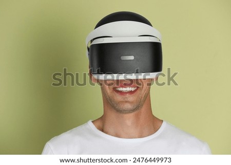 Smiling man using virtual reality headset on light green background