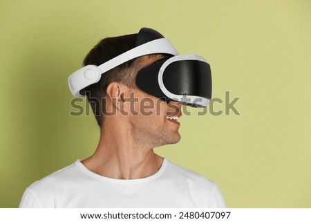 Smiling man using virtual reality headset on light green background
