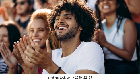 Smiling Man Watching A Soccer Match And Applauding At Stadium. Excited Sports Fans Applauding And Celebrating Their Team's Victory.
