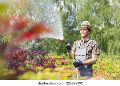 Smiling man watering plants at garden - Powered by Shutterstock