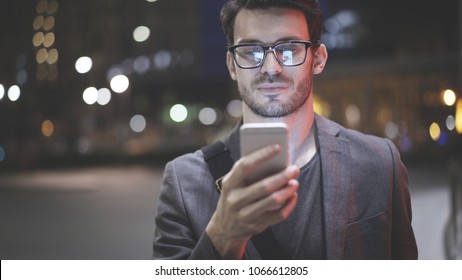 A smiling man wearing eyeglasses is holding scrolling texting in his cellphone. A smiling man calls for a taxi in an app. - Powered by Shutterstock